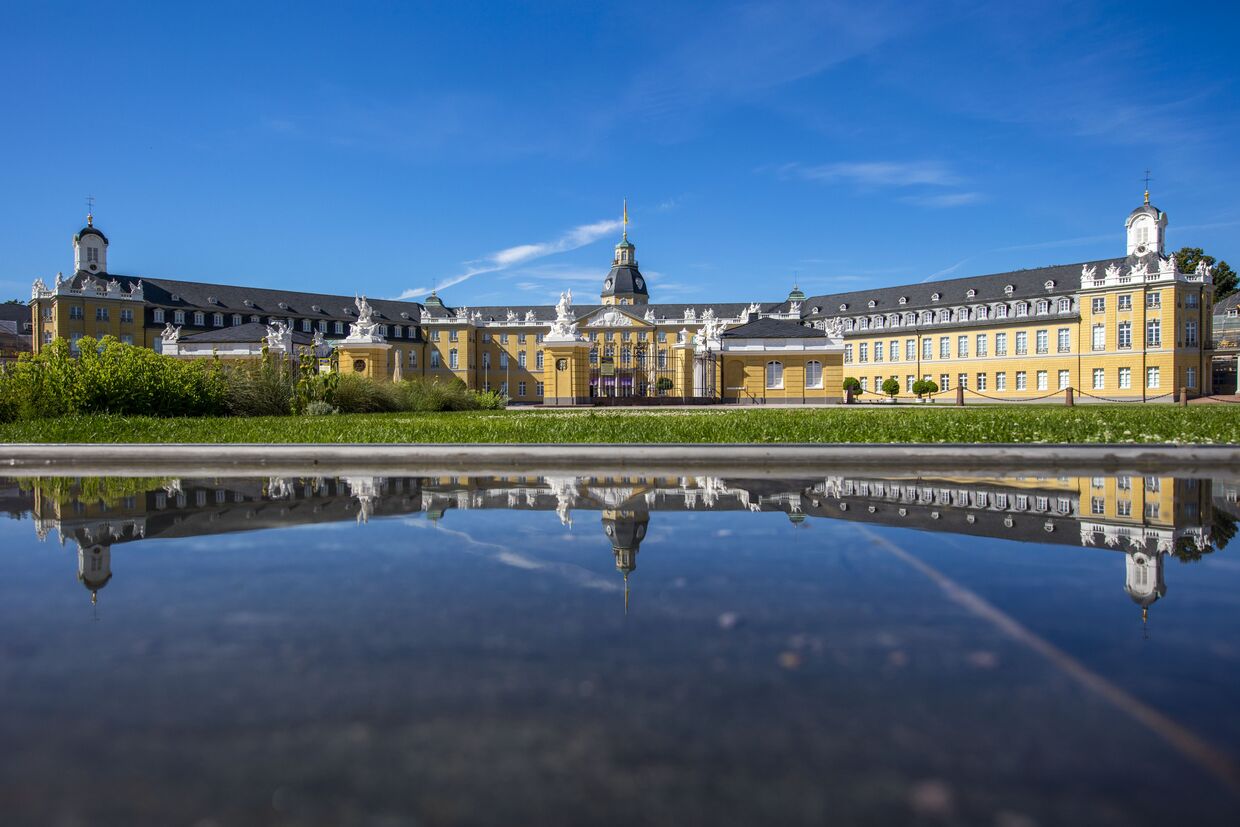 Totale des Schloss Karlsruhe bei strahlend blauem Himmel, gespiegelt im Wasser des Brunnens vor dem Schloss